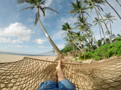 A coffee shop owner relaxes in a hammock on a tropical beach.