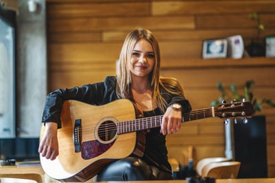Young female singer holding a guitar inside a coffeehouse.