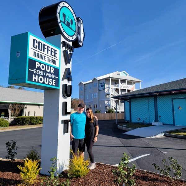 Owners Jeff Hogan and Jenn Taylor pose with sign outside The Vault Coffee and Pour House in Carolina Beach, North Carolina